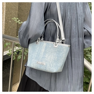 Detail of light blue sequin tote bag with silver handles worn by a model in gray