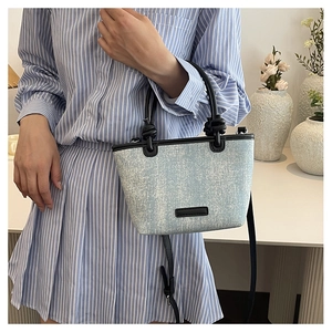 Close-up of light blue sequined canvas bucket bag with black leather handle details