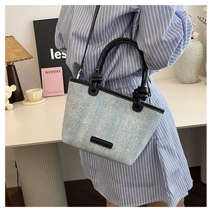 Detail shot of a light blue denim textured tote bag with black leather straps and trim