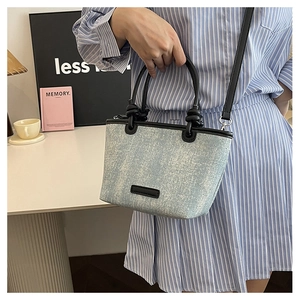 Detail of light blue denim bucket bag with black leather trim and detachable shoulder strap