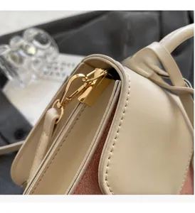 Detail of contrast stitching, gold metal clasp, and textured leather on a shoulder bag