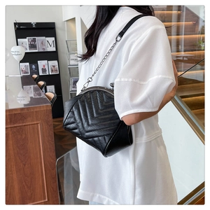 Detail of black quilted shell bag with V-shaped stitching and vintage metal chain strap