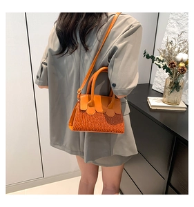 Close-up of orange faux leather handbag with crocodile pattern and adjustable strap