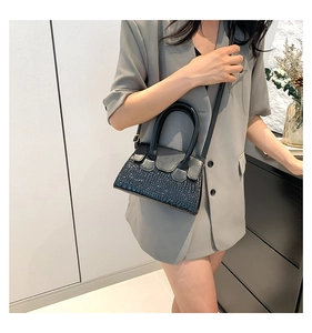 Close-up of black crossbody bag with crocodile texture worn with a grey blazer