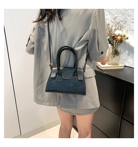 Close-up of black small square bag with crocodile pattern worn with a grey blazer