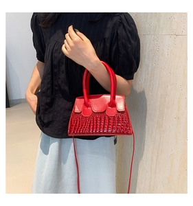 Close-up of red leather handbag with crocodile pattern held by model for elegant style