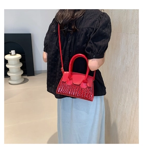 Detailed view of red crocodile-patterned leather crossbody bag worn by a model