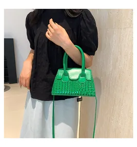 Detail of green crocodile pattern handbag with top handle and slim shoulder strap