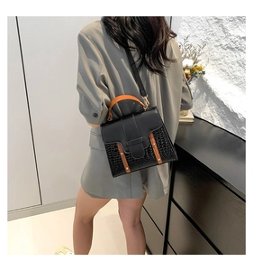 Détail du sac noir à texture crocodile avec anse orange porté à l'épaule du modèle