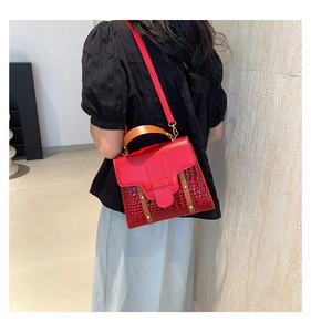 Détail d'un sac à main rouge crocodile avec ferrures dorées et poignée en cuir marron