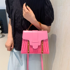 Sac à main rose à motif crocodile avec poignées marron et rivets dorés sur fond beige