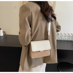 Detail view of the wide shoulder strap and gold hardware on a two-tone crossbody bag