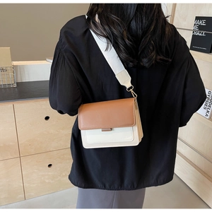 Detail of a brown and cream color-block crossbody bag with wide woven strap