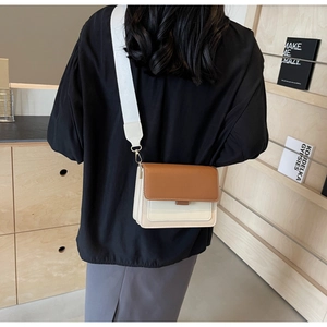 Detail view of a color-block crossbody bag with a wide fabric shoulder strap worn by a model