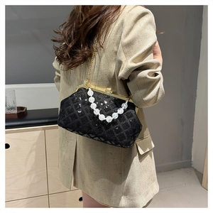 Detail of black sequin clutch bag with pearl handle and golden chain on beige suit