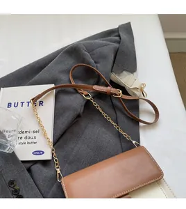 Close-up of contrast stitching on a two-tone leather crossbody bag with chain and wide straps