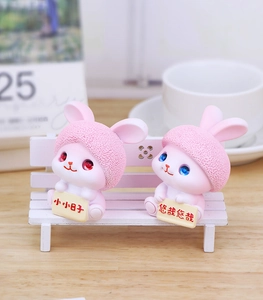 Close-up of pink resin rabbit figurines with crystal eyes on a white mini bench decor