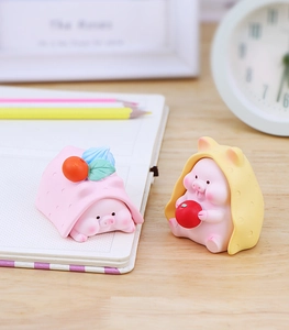 Close-up of cute pink resin pig figurines with fruit details on a cozy wooden desk