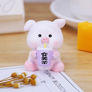 Cute pink resin pig figurine holding a purple cup as a desk ornament on wooden surface