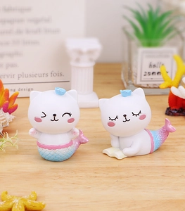 Détail de figurines de chat sirène en résine avec écailles dégradées sur table en bois