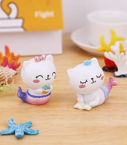 Détail de deux figurines de chat sirène en résine avec queue dégradée sur une table en bois