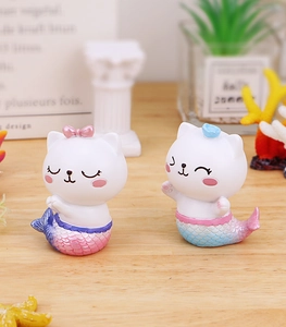 Détail de figurines de chat sirène en résine pastel sur un bureau en bois clair