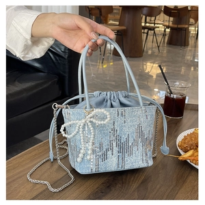 Detail of light blue bucket bag with sequins, pearl bow, and chain strap in cafe setting