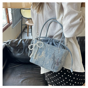 Close-up of light blue canvas bucket bag featuring silver sequins and pearl bow charm
