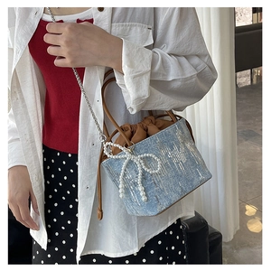 Detail of light blue bucket bag with sequins, leather handle, and pearl bow charm