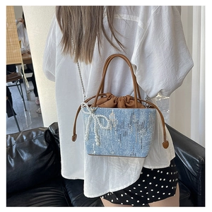 Detail of light blue denim bucket bag featuring silver sequins and pearl bow charm