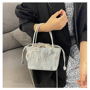 Detailed shot of sequin bucket bag featuring a pearl bow charm and drawstring closure