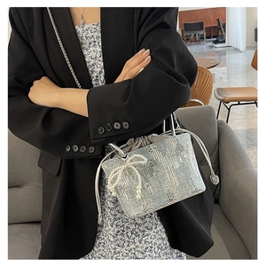 Detail of silver sequin handbag with pearl bow charm and chain strap on a model