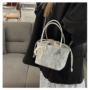 Close-up of sequin bucket bag with pearl bow pendant and metal chain strap on model