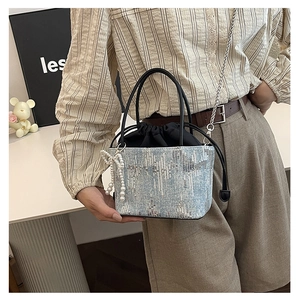 Detail of sequin bucket bag featuring white pearl bow charm and black leather handle