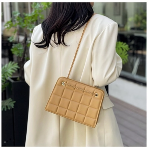 Detailed side view of yellow quilted chain bag with grid texture on white blazer