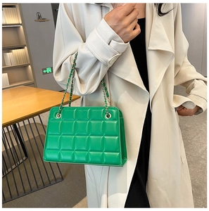 Detail of vibrant green quilted crossbody bag with golden chain strap on a trench coat