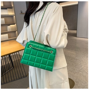 Detail of green quilted crossbody bag with gold chain strap on a model shoulder