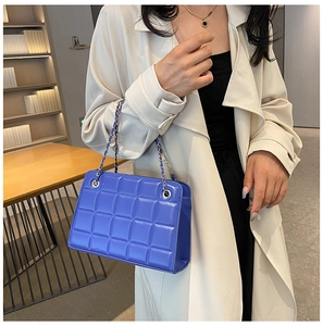 Blue quilted chain bag worn by model with beige trench coat in warm indoor lighting