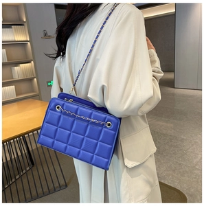 Close-up of blue quilted leather bag with gold chain strap on a trench coat