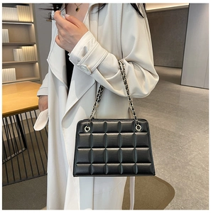 Detail of black quilted leather shoulder bag with gold chain strap on a trench coat
