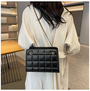 Detail of black quilted leather shoulder bag with gold-tone metal chain on female model