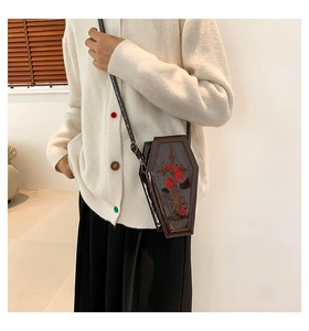 Detail of cross and red rose embroidery on a high-gloss brown coffin-shaped bag