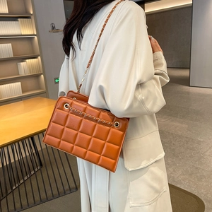 Caramel brown quilted crossbody bag with gold chain strap shown in an elegant bookstore