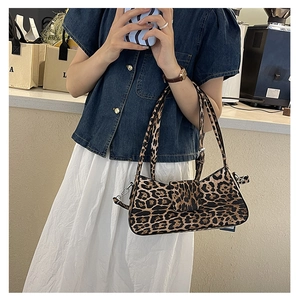 Model wearing a leopard print baguette underarm bag in a cozy coffee shop setting