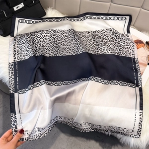 Detail of silk scarf with leopard print and chain pattern on white plush carpet