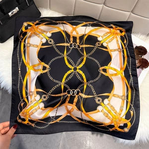Luxury square silk scarf with golden chain pattern on plush white carpet with accessories