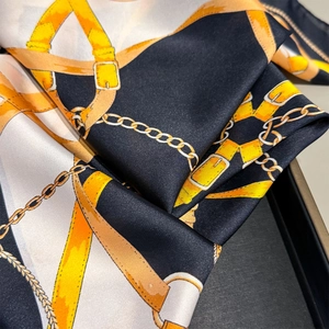 Close-up of luxury silk scarf showing golden chain and leather belt pattern on satin fabric