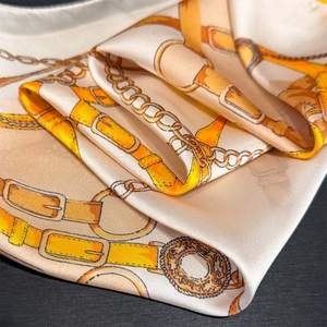 Close-up of golden chain and belt pattern on luxurious cream silk scarf fabric