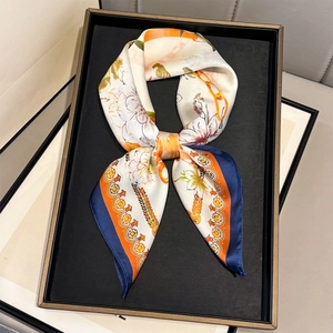 Floral silk scarf with orange petals and equestrian chain pattern on a display tray