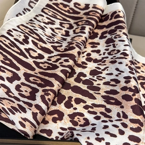 Detailed view of leopard print silk scarf texture with glossy satin finish and white borders